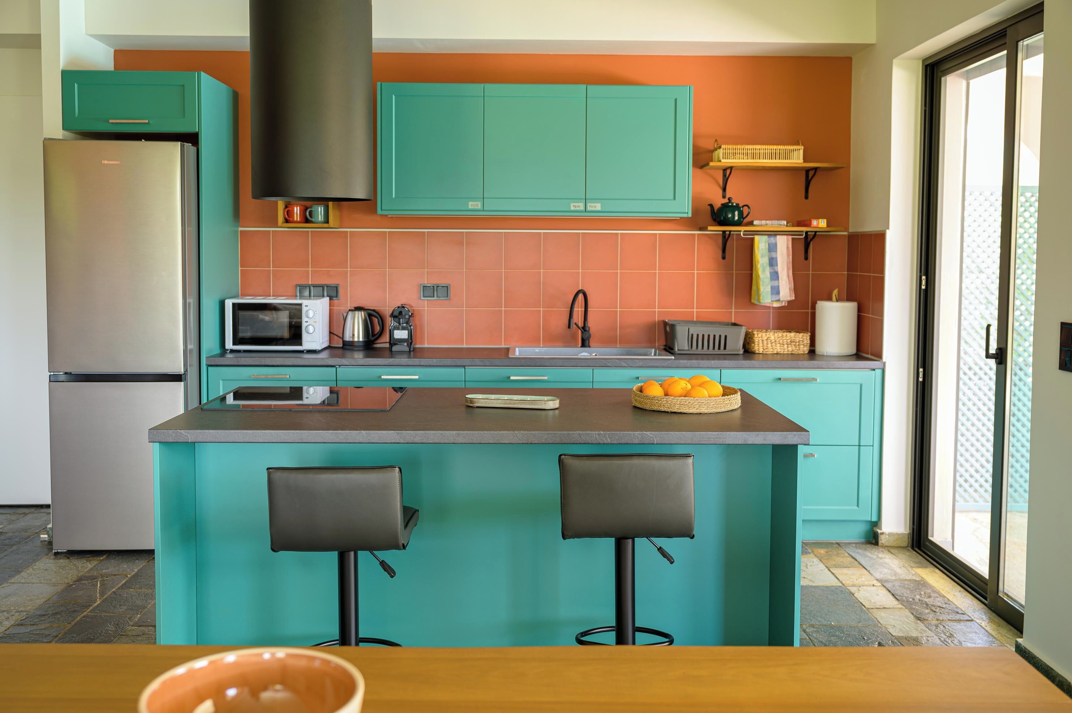 Una cocina con armarios color turquesa, una isla central con taburetes, un refrigerador, un microondas y un tostador.