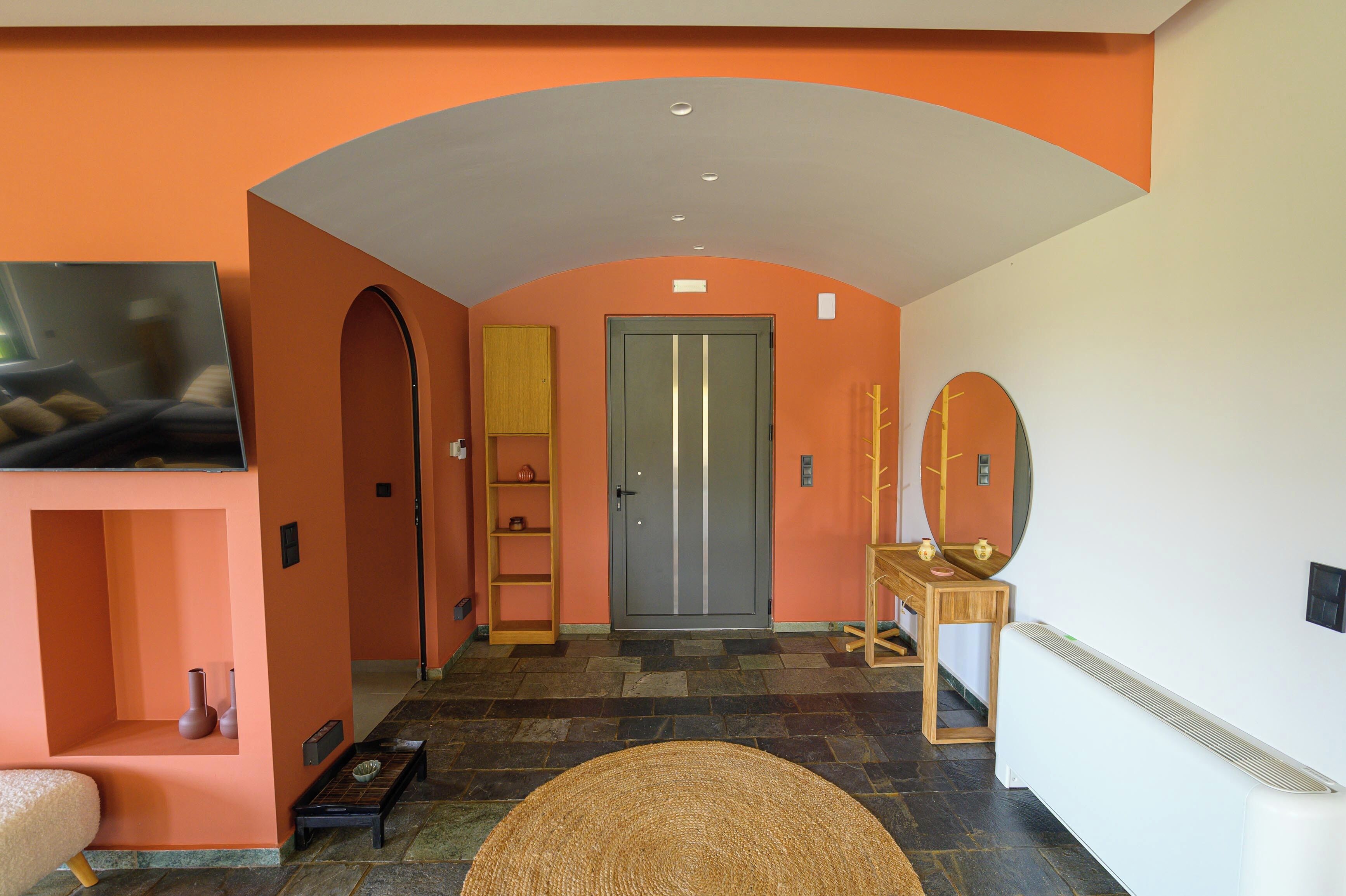 A hallway with an arched ceiling, a television, a door, a mirror, and a small table with a vase.