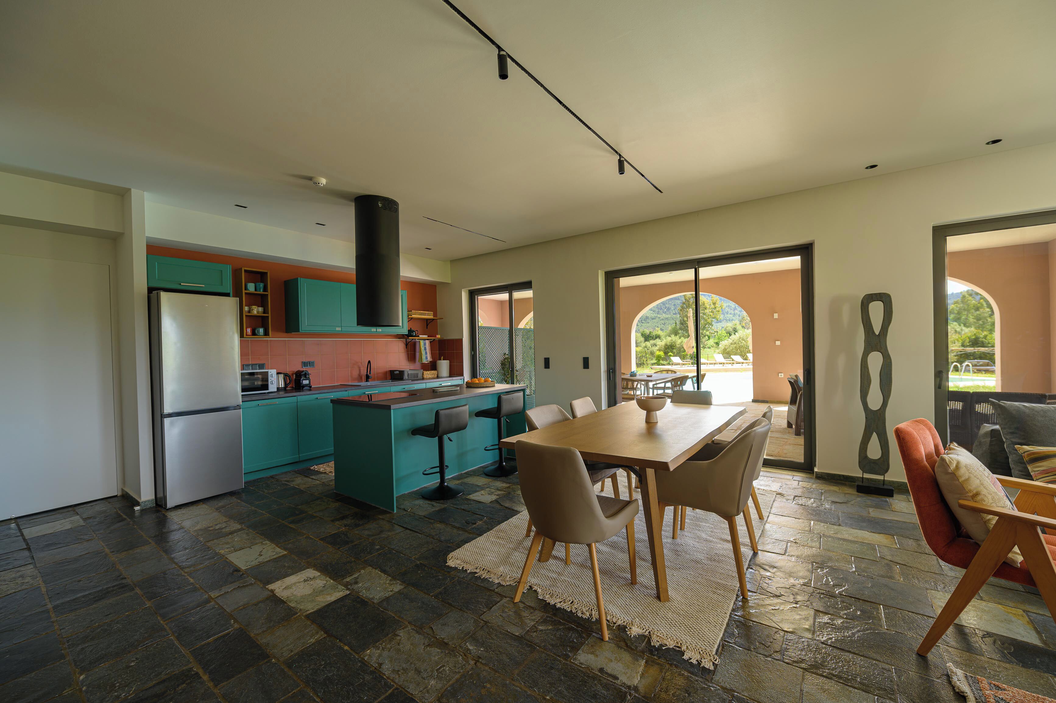 A modern kitchen with teal cabinets, a central island, and a dining area with a table and chairs.