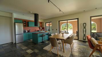 A modern kitchen with teal cabinets, a central island, and a dining area with a table and chairs.
