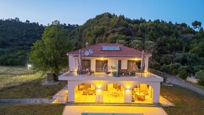 Ein zweigeschossiges Haus mit Swimmingpool, einem Balkon mit Gartenmöbeln und Blick auf einen bewaldeten Hügel.