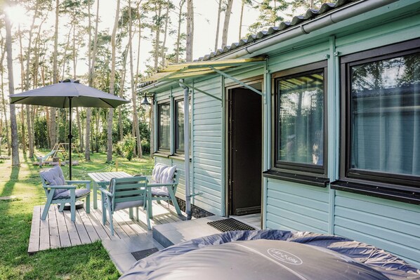 A light blue cabin with a deck, two chairs, and a table.