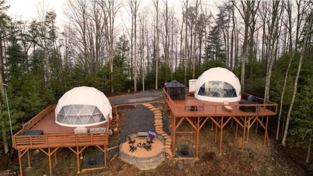 Twee koepelvormige cabins met houten terrassen, omringd door een bos.