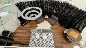 Een tentvormige kamer met een ronde lamp, twee banken, een kleine tafel en een gestreept voetenbankje.