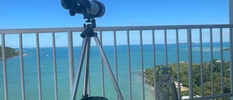 Un télescope installé sur un balcon, offrant une vue sur l’océan et la côte lointaine.