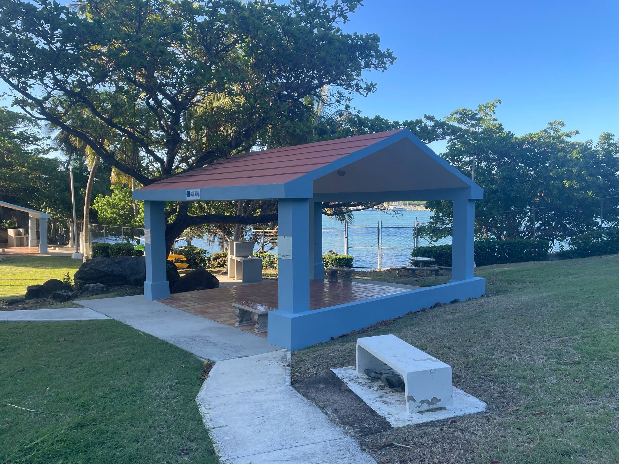 A gazebo with a red roof and blue walls, located on a grassy area with a view of the water.