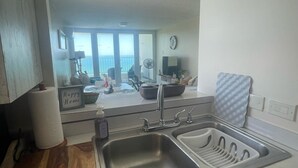 A kitchen with a stainless steel sink, a wooden countertop, and a view of a balcony with a pool. - Ocean View 2 Bed 1 Bath 2 Parkings Pool (Fajardo)