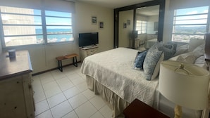 A bedroom with a bed, a TV, a desk, and a window with a view of the sea. - Ocean View 2 Bed 1 Bath 2 Parkings Pool (Fajardo)