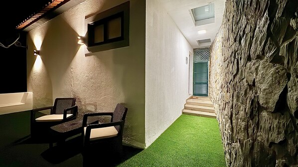 A modern outdoor seating area with two chairs and a table, a textured wall, and a tree trunk.