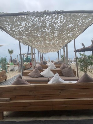 Zona de estar frente a la playa, con bancos de madera y sombrillas de paja que dan sombra.
