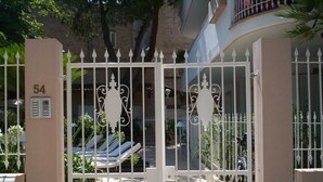 Un ingresso recintato con un cartello numerico, una zona piscina con lettini e un edificio sullo sfondo con balconi.