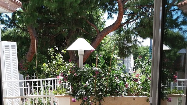 Una veranda esterna con due tavoli in vimini, una decorazione a stella marina rossa e un ombrellone bianco.