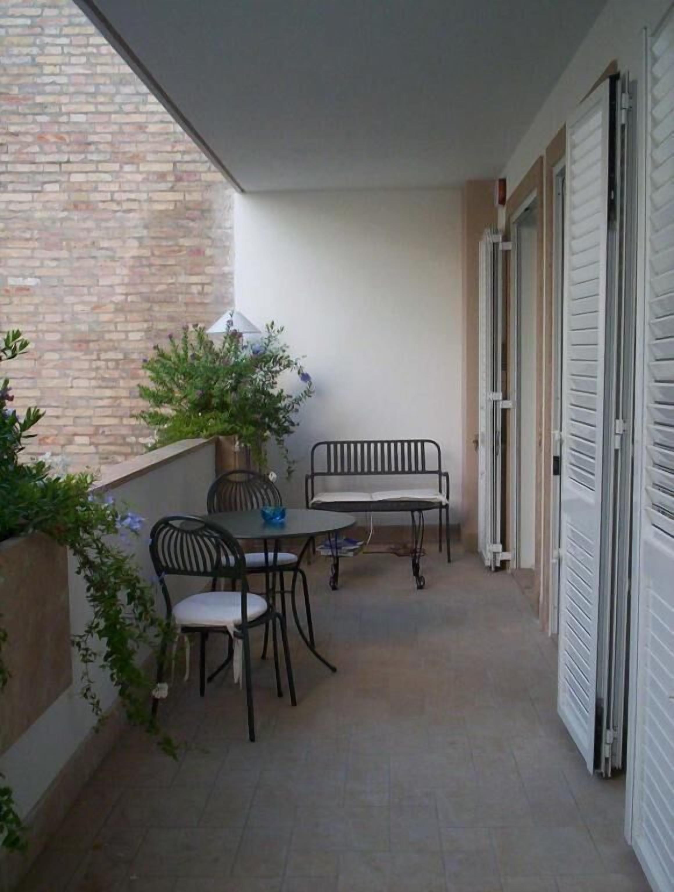 A small outdoor balcony with a table and two chairs, a potted plant, and a closed door.