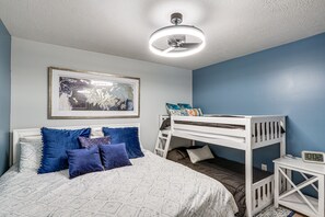Una camera da letto con un letto a castello, un comodino con una sveglia, un quadro appeso alla parete e una ventola a soffitto.