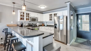 A modern kitchen with white cabinets, stainless steel appliances, and a bar area with stools. - Lakefront Retreat w/ Community Pool in Osage Beach (Osage Beach)