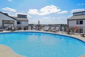 Una piscina con lettini e ombrelloni, circondata da edifici con vista sull'acqua.
