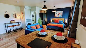Ein modernes Wohnzimmer mit einem Holzespeisetisch, einem blauen Sofa und einem Bett mit orangefarbener Bettwäsche.