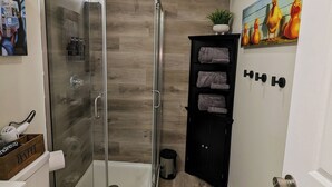 Un baño moderno con ducha envuelta en vidrio, inodoro y un mueble negro con toallas.
