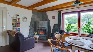 A cozy room with a stone fireplace, wooden beams, wicker furniture, and a view of greenery outside.