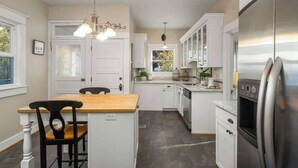 A kitchen with white cabinetry, a wooden island, a stainless steel refrigerator, and a hanging light fixture. - Paradise Haven-95 walk score-Dedicated Workspaces (Portland)