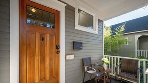 A wooden front door with a glass panel, a mailbox, and two wicker chairs on a porch with a white railing. - Paradise Haven-95 walk score-Dedicated Workspaces (Portland)