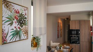 Ein Essbereich mit einem Holztisch, gedeckt für vier Personen, einer Vase mit grünen Blättern und einem Blumenbild an der Wand.