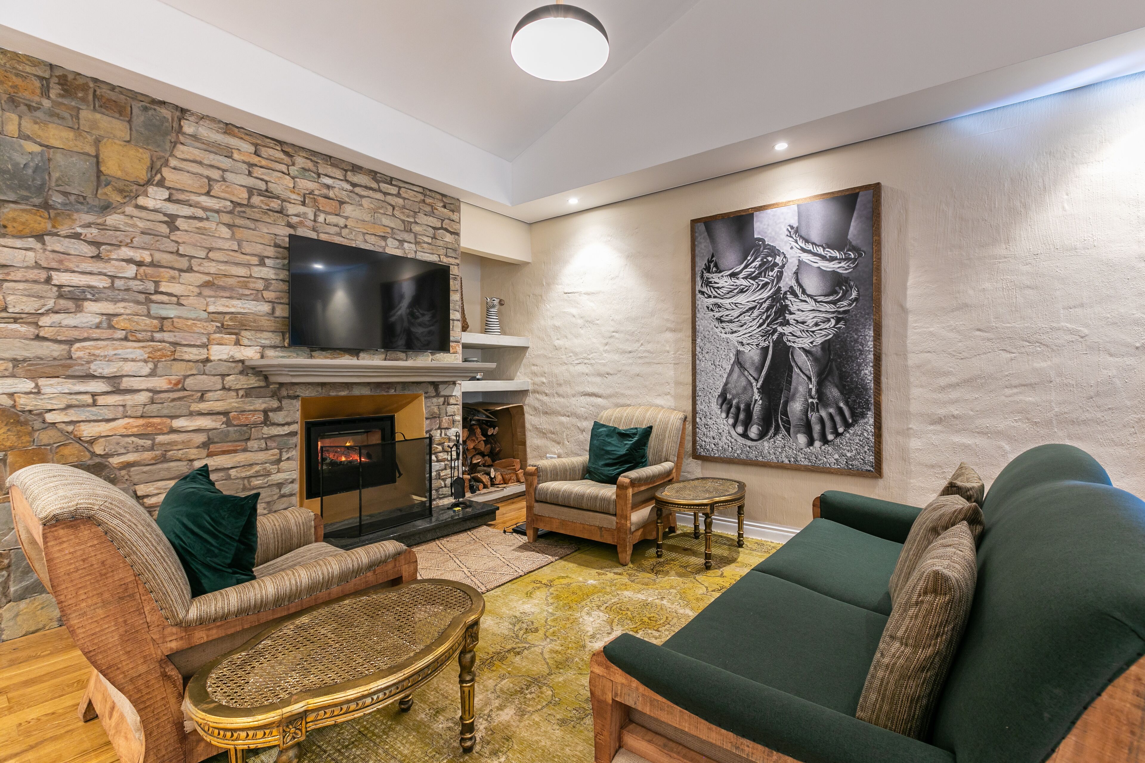 Un salon chaleureux avec une cheminée en pierre, des fauteuils confortables et un grand tableau abstrait.