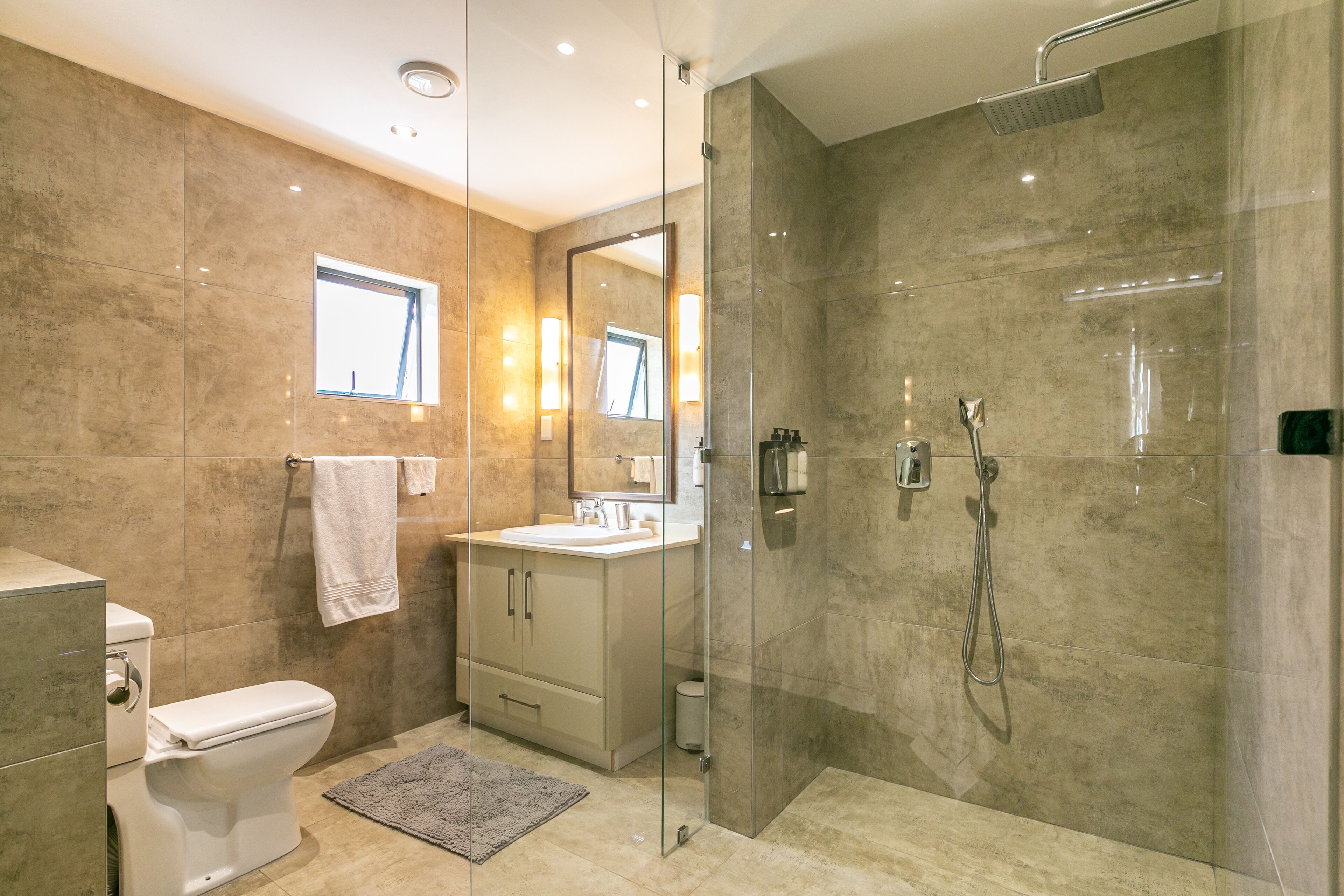 Un baño moderno con ducha envuelta en vidrio, inodoro, lavamanos y tocador.