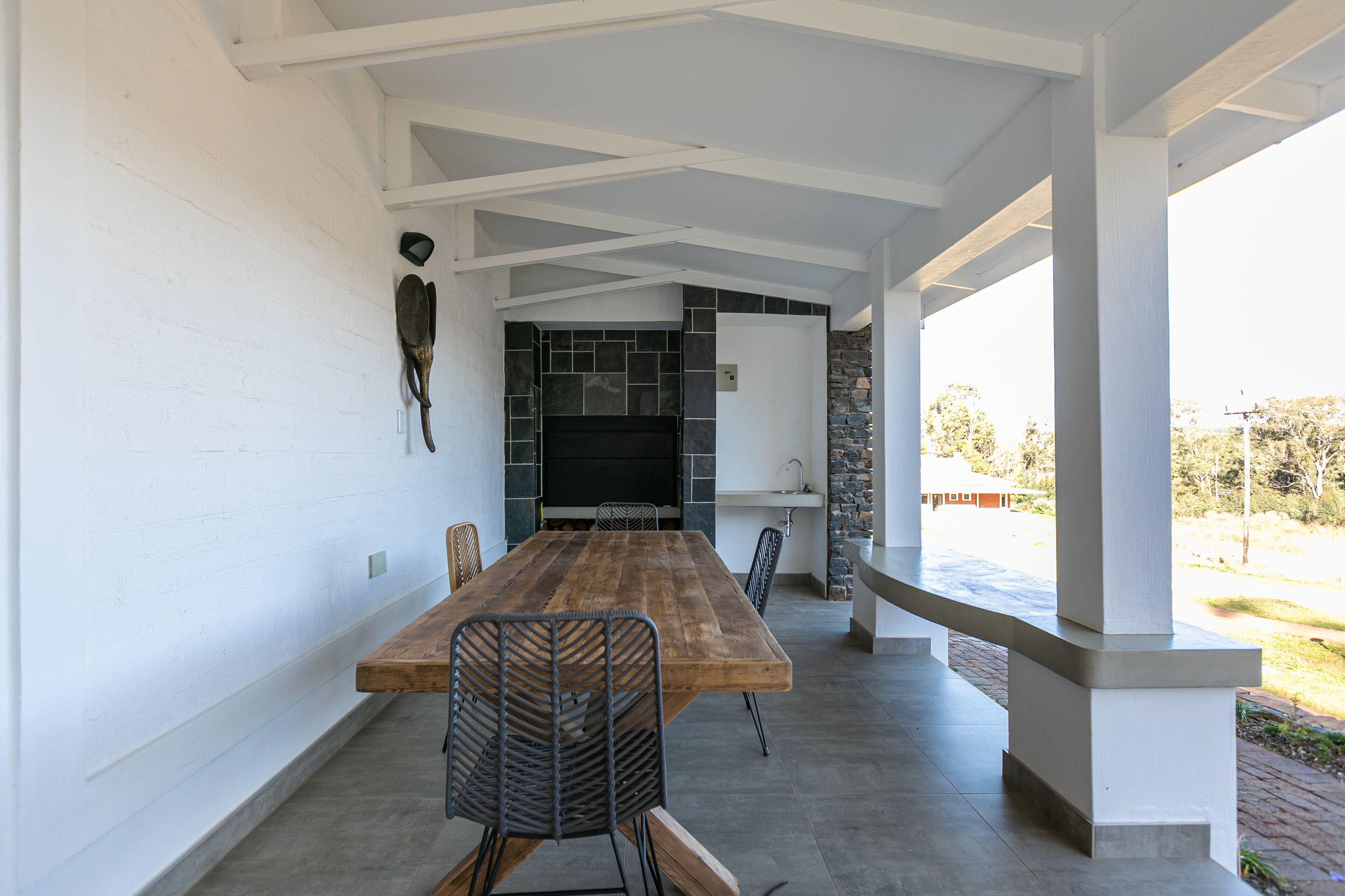 A long wooden table with chairs, a stone fireplace, and a white wall with a mounted object.