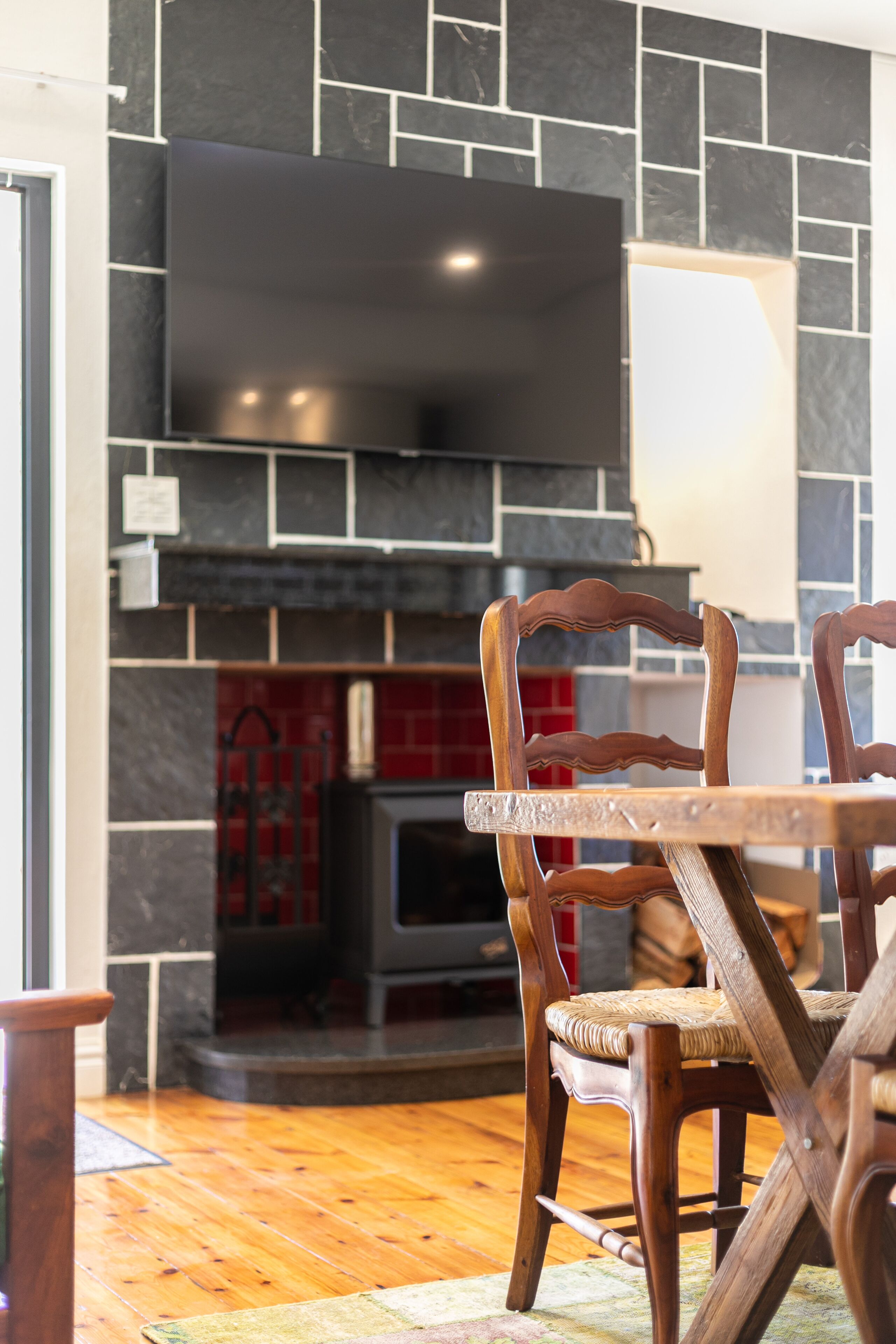 A modern kitchen with a built-in TV, stone backsplash, and wooden chairs around a table.