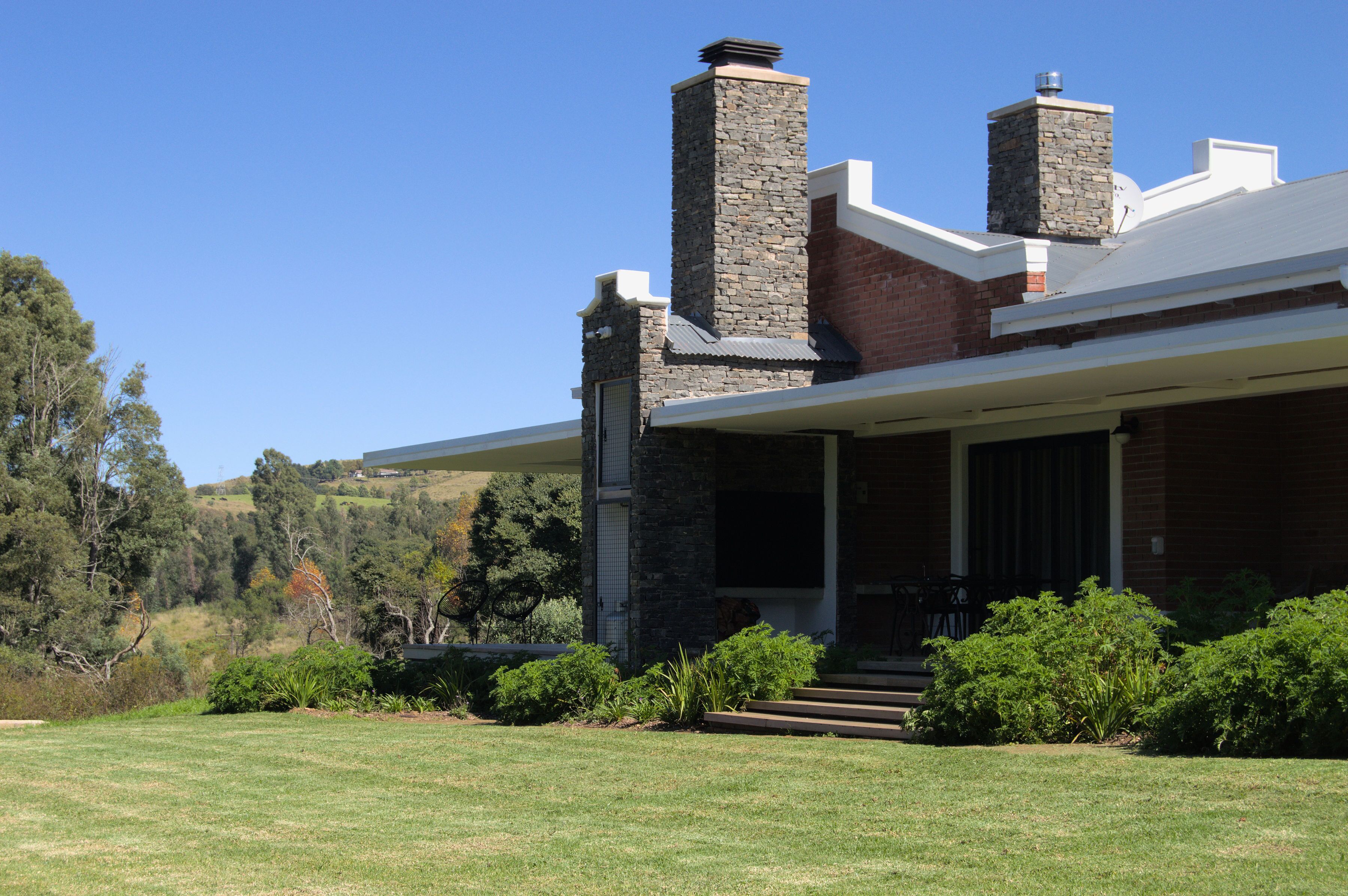 A modern house with a stone chimney, a covered porch, and a well-maintained lawn.