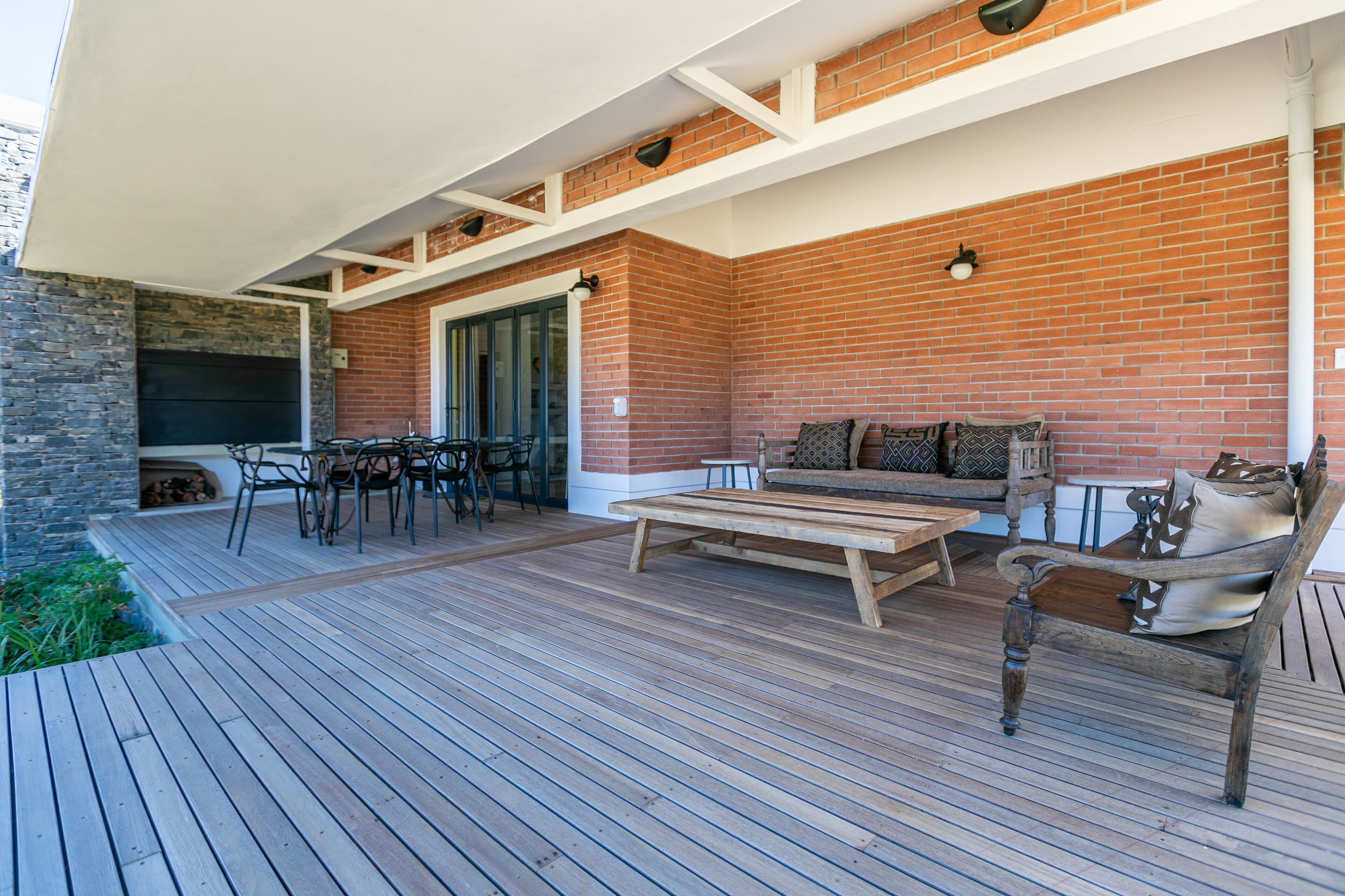 Terraza de madera con pared de ladrillo, mobiliario exterior y una mesa.