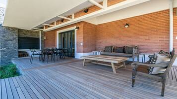 Terraza de madera con pared de ladrillo, mobiliario exterior y una mesa.