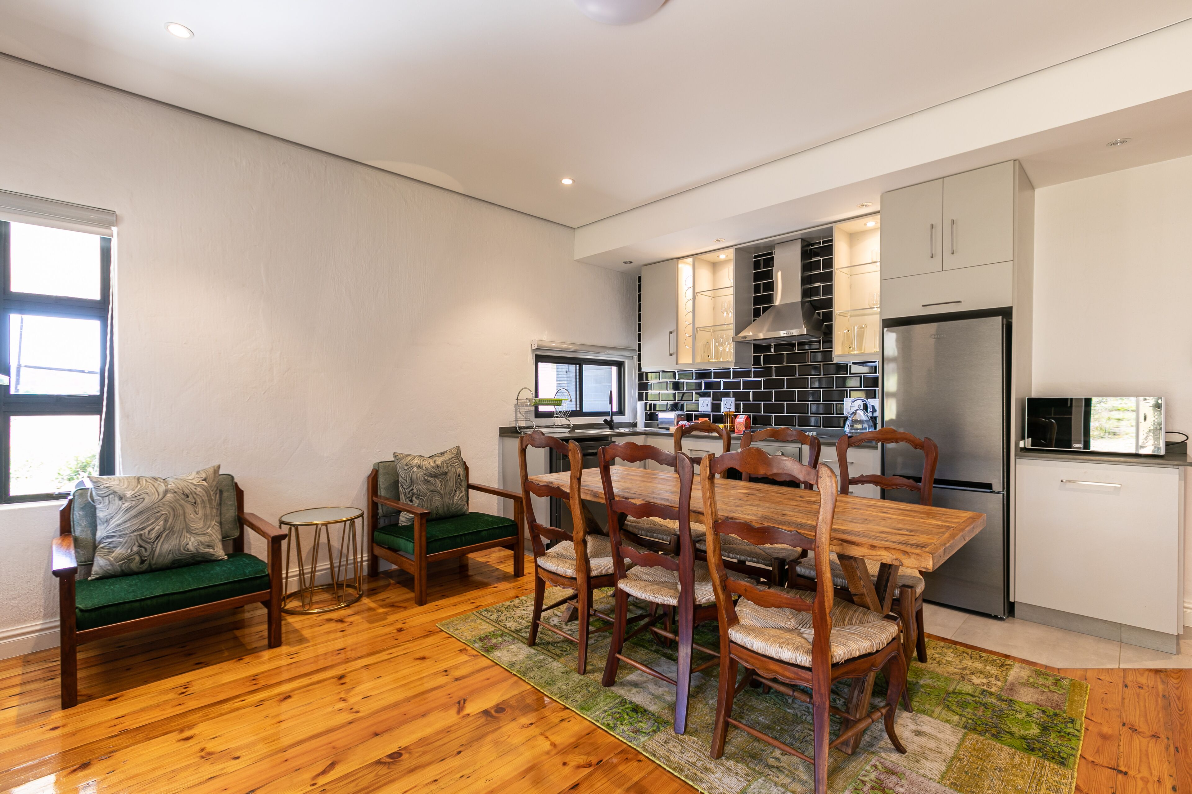 A modern kitchen with a dining area, wooden furniture, and a large refrigerator.
