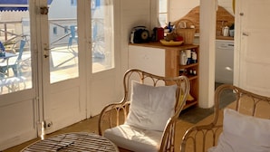 Ein Zimmer mit Korbmöbeln, einem Tisch und einer Küchenzeile mit Kühlschrank und Regalen.