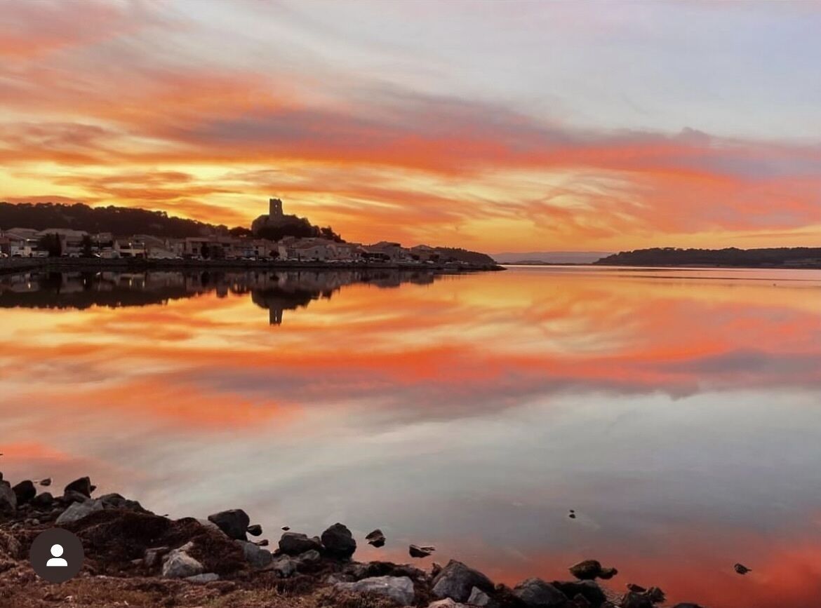 Un lago tranquilo que refleja un atardecer con edificios en la orilla.