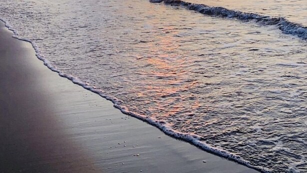 Ein Strand bei Sonnenuntergang, sanfte Wellen umspülen das Ufer.