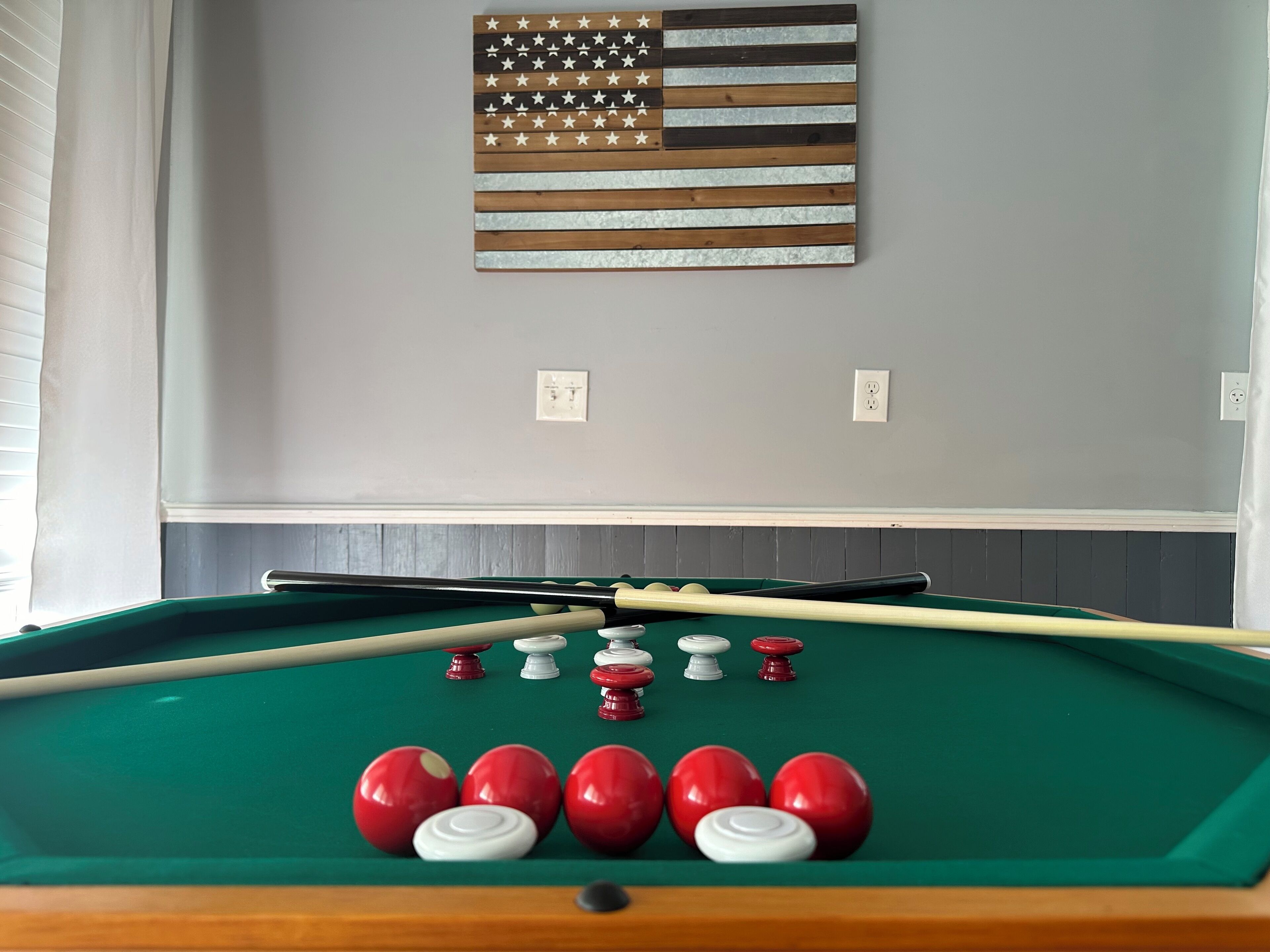 Ett biljardbord med röda och vita bollar, ett biljardkö och en trädekoration i form av en amerikansk flagga på väggen.