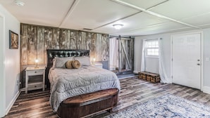 A bedroom with a large bed, wooden panel wall, a nightstand, a suitcase, and a door. - New Hope Bourbon Stop- historic home, peaceful spot in heart of Bourbon country (New Hope)