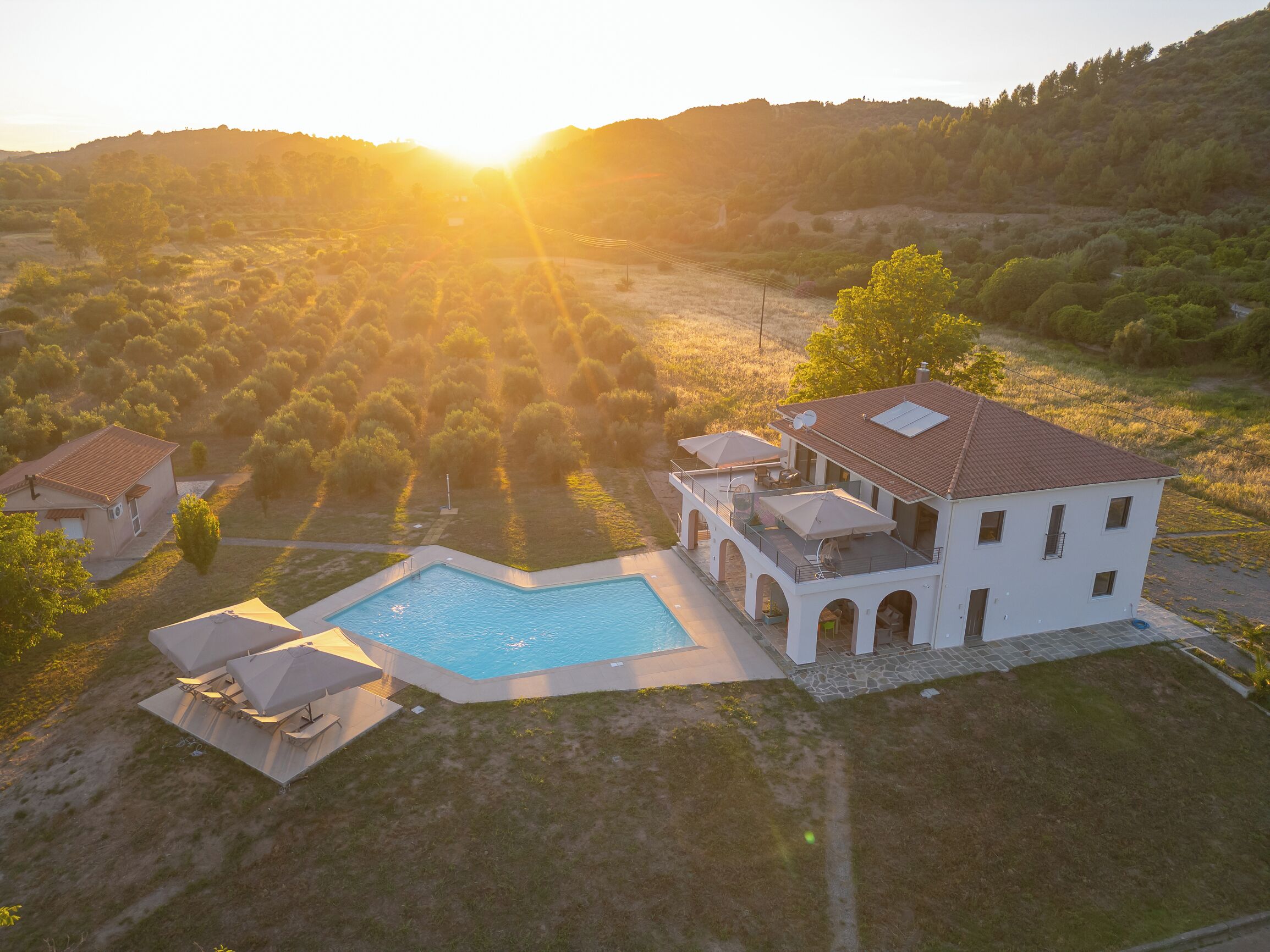 A large house with a swimming pool, surrounded by a hilly landscape.