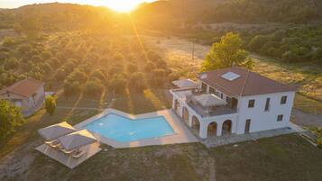 A large house with a swimming pool, surrounded by a hilly landscape.