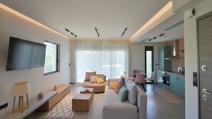 A modern living room with a sofa, coffee table, and TV. There is a kitchen area with cabinets and a dining table. - Antinea Olympian Villa East studio (Archea Pissa)