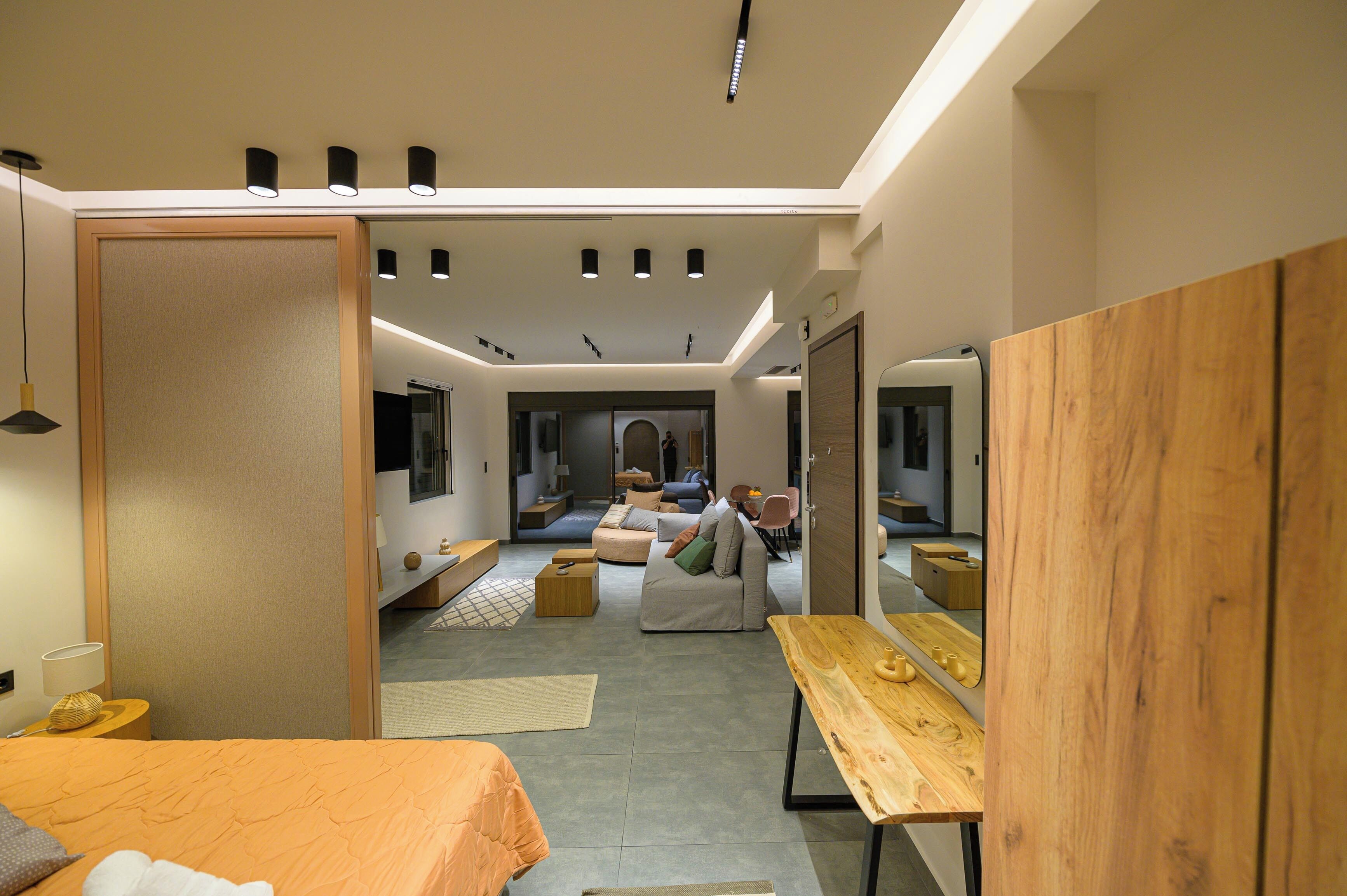 A modern hotel room with a bed, a wooden table, a sofa, and a TV.