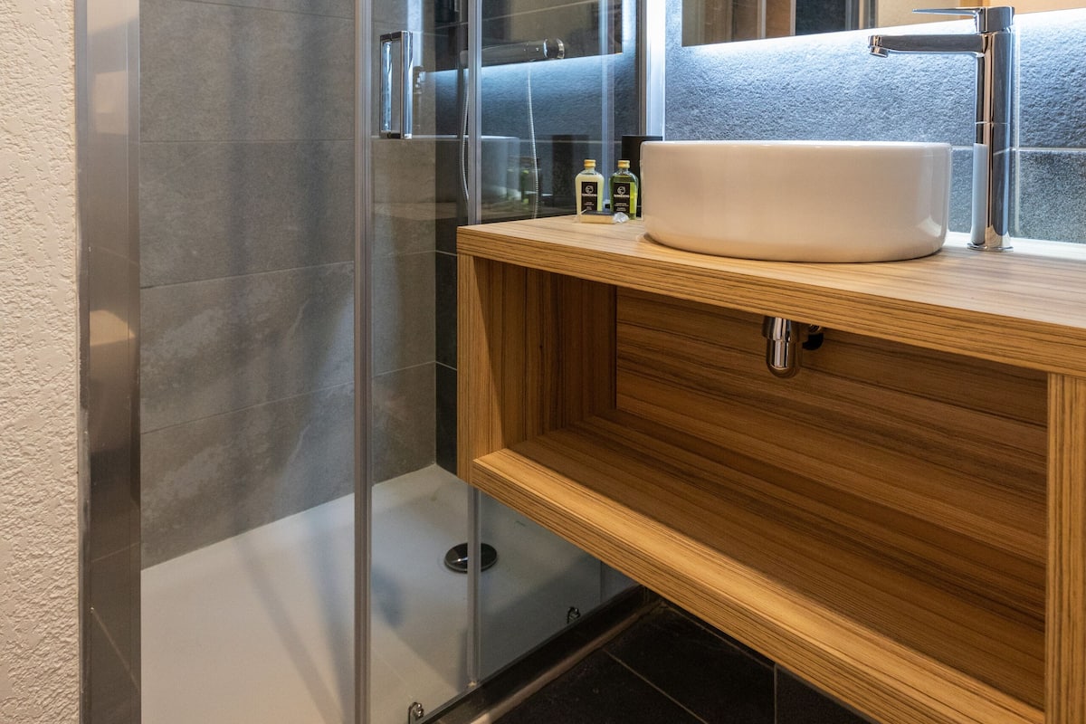 A modern bathroom with a glass-enclosed shower, a wooden vanity with a sink, and a large mirror.