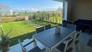 An outdoor patio with a table and chairs, a potted plant, and a view of a green landscape and buildings in the distance.