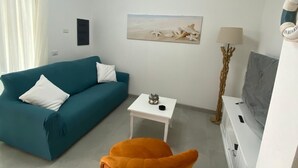 A modern living room with a teal sofa, an orange chair, a white coffee table, and a flat-screen TV.