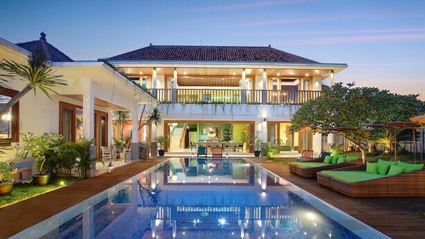 Una casa de dos pisos con piscina, mobiliario exterior y un balcón.