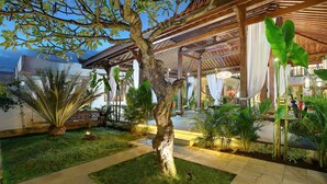 Un espacio exterior bien cuidado, con un árbol central rodeado de plantas diversas y una zona de estar cubierta.