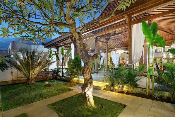A well-maintained outdoor area with a central tree, surrounded by various plants and a covered seating area.