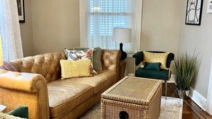 Un salon avec un canapé en cuir marron, un fauteuil vert, une table basse en osier et un tapis à motifs.